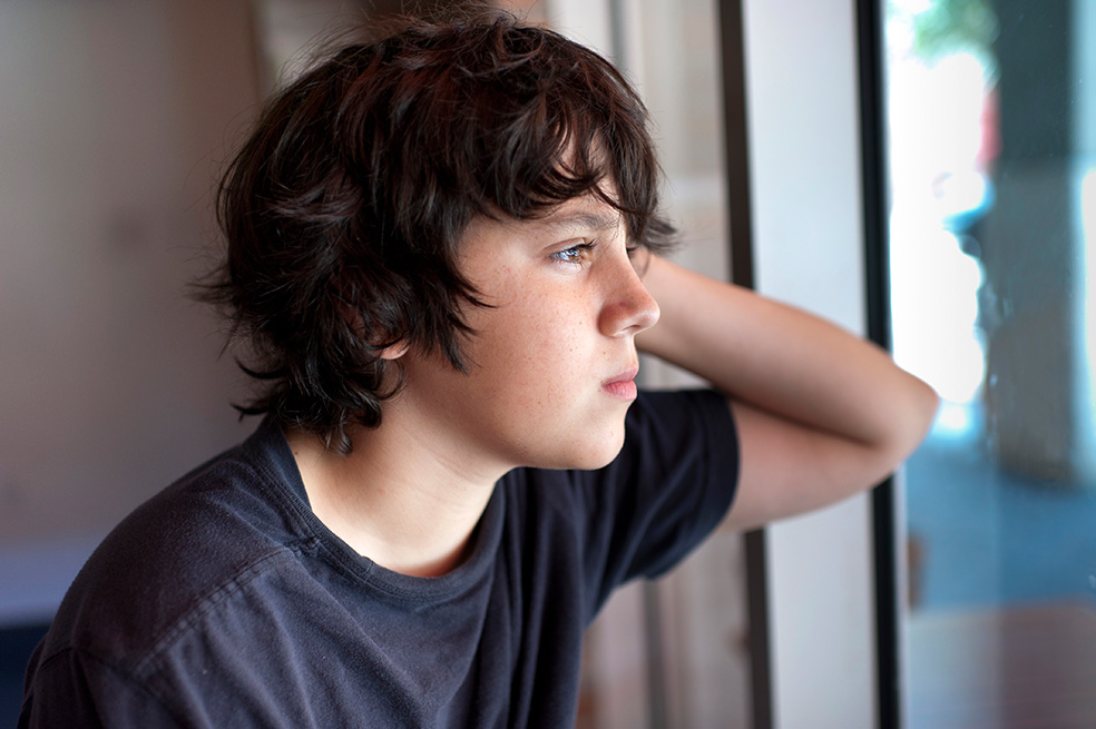 Ein Teenager schaut ernst aus dem Fenster.
