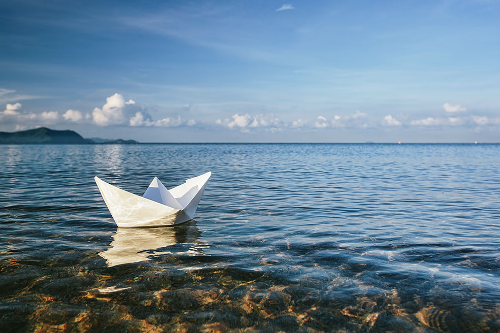 Ein Papierschiff schwimmt in der Sonne auf eine großen See.